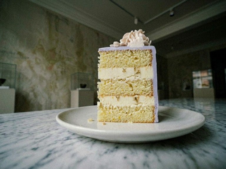 A slice on a plate showing the pale sponge layers beneath the periwinkle glaze, in the gallery