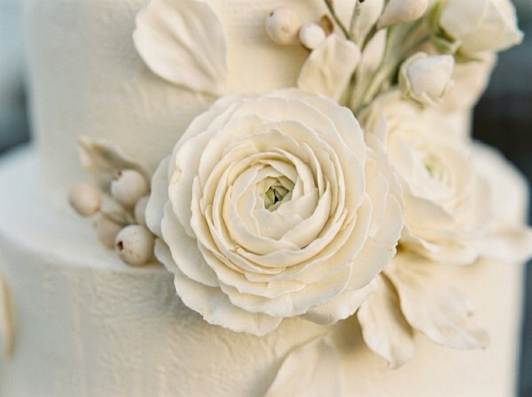 Close detail of a hand-piped ivory sugar ranunculus and berries on the textured tier