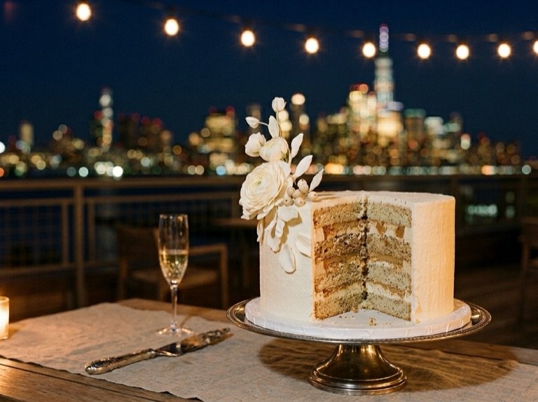 A cut tier revealing the layered sponge and cream, with sugar flowers, on a rooftop at night